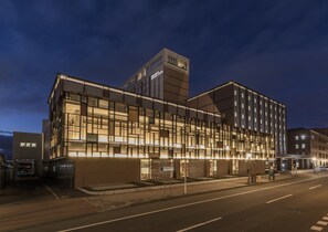 Un hotel moderno con fachada de vidrio, base de ladrillo y una torre destacada.
