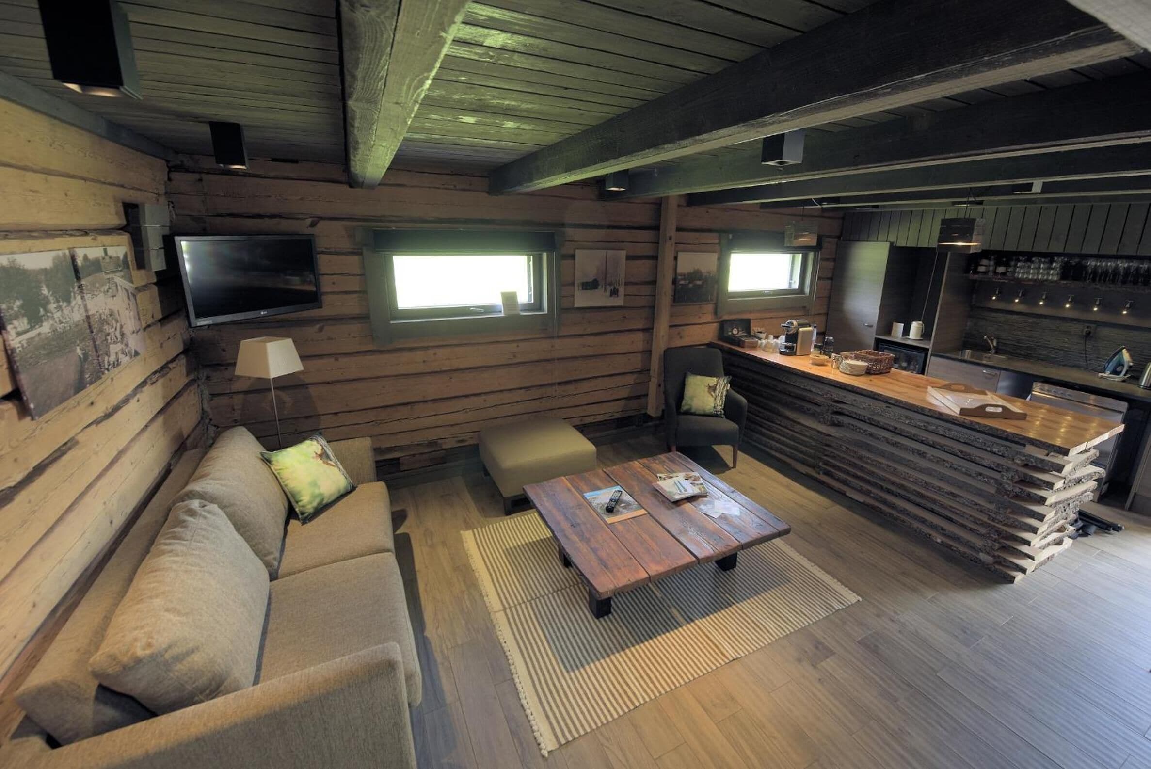 Una habitación acogedora de estilo cabaña, con detalles de madera, un sofá, una mesa de centro, un televisor montado en la pared y una zona de bar con mostrador y estanterías.