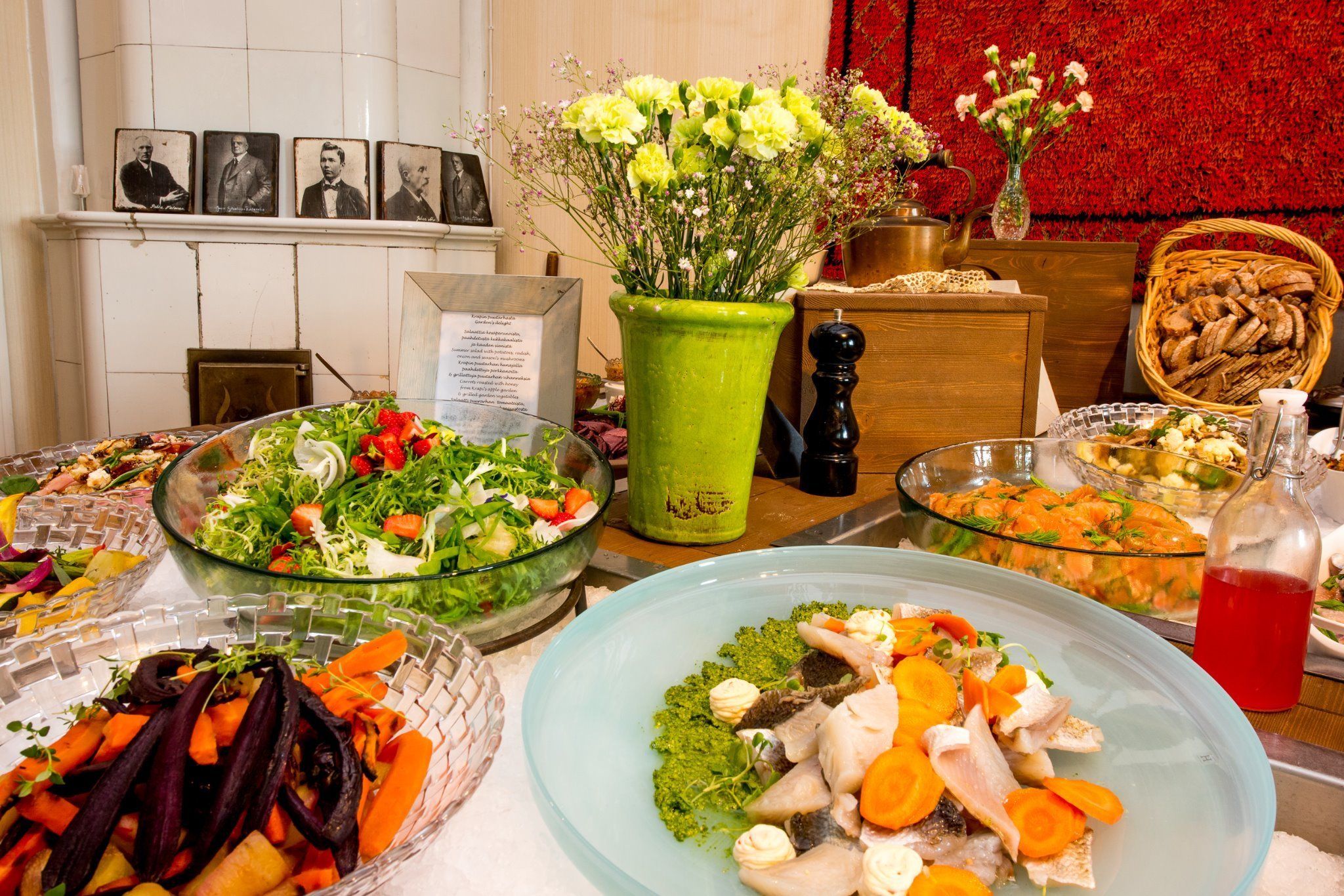 Une table de buffet garnie de divers plats, un vase vert rempli de fleurs et un mur décoré de motifs floraux rouges.