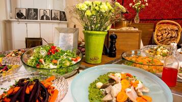 Une table de buffet garnie de divers plats, un vase vert rempli de fleurs et un mur décoré de motifs floraux rouges.
