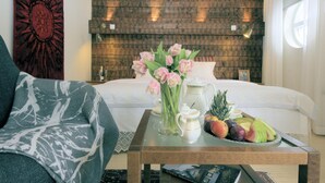 Et pænt opredt soveværelse med seng, et natbord med frugtfat, en vase med blomster og et magasin.