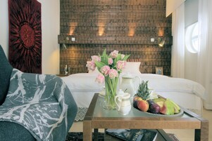 Un dormitorio ordenado con una cama, una mesita de noche con una bandeja de frutas, un jarrón de flores y una revista.
