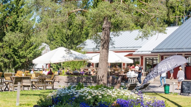 Et udendørs siddeområde med træborde og stole, omgivet af en blomsterbed med forskellige blomster.
