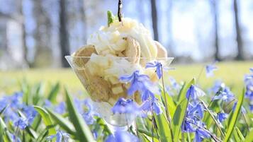 A bowl of ice cream with a mint leaf on top, placed on grass with blue flowers around.