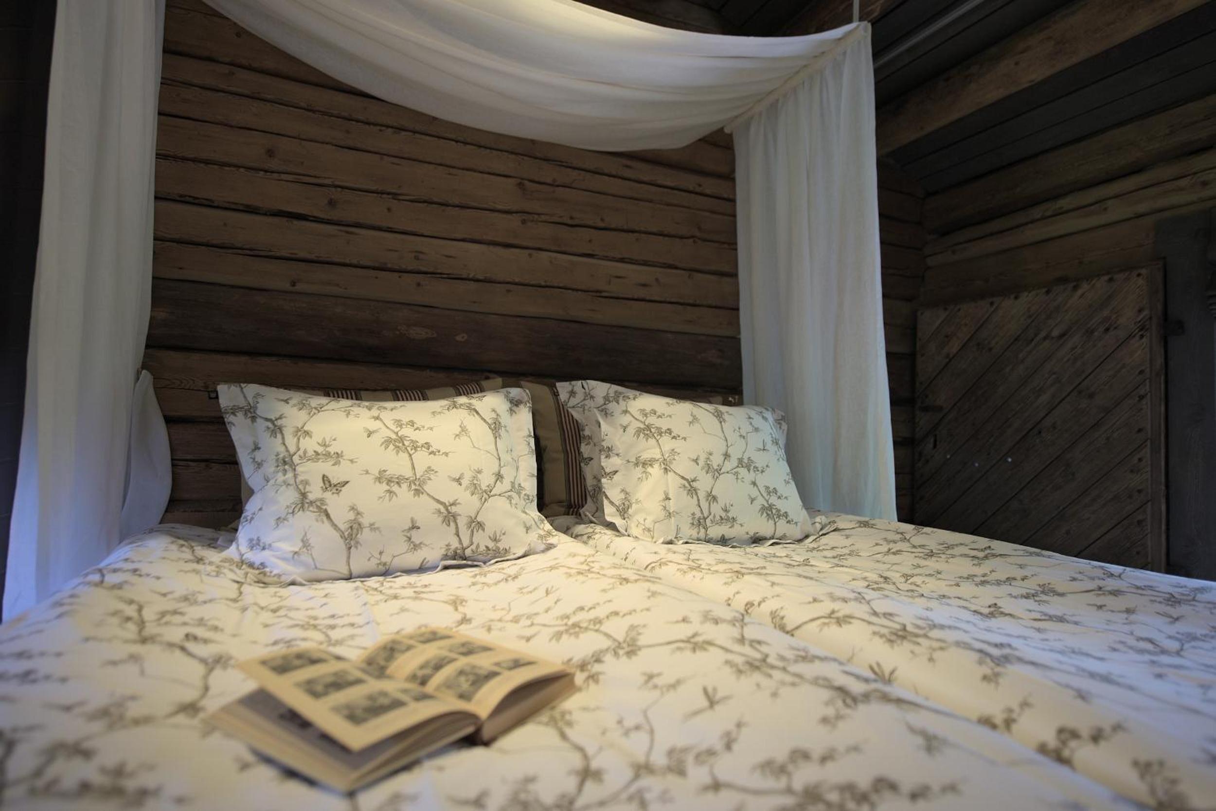 A wooden cabin bedroom with a canopy bed, floral bedding, and an open book on the bed.