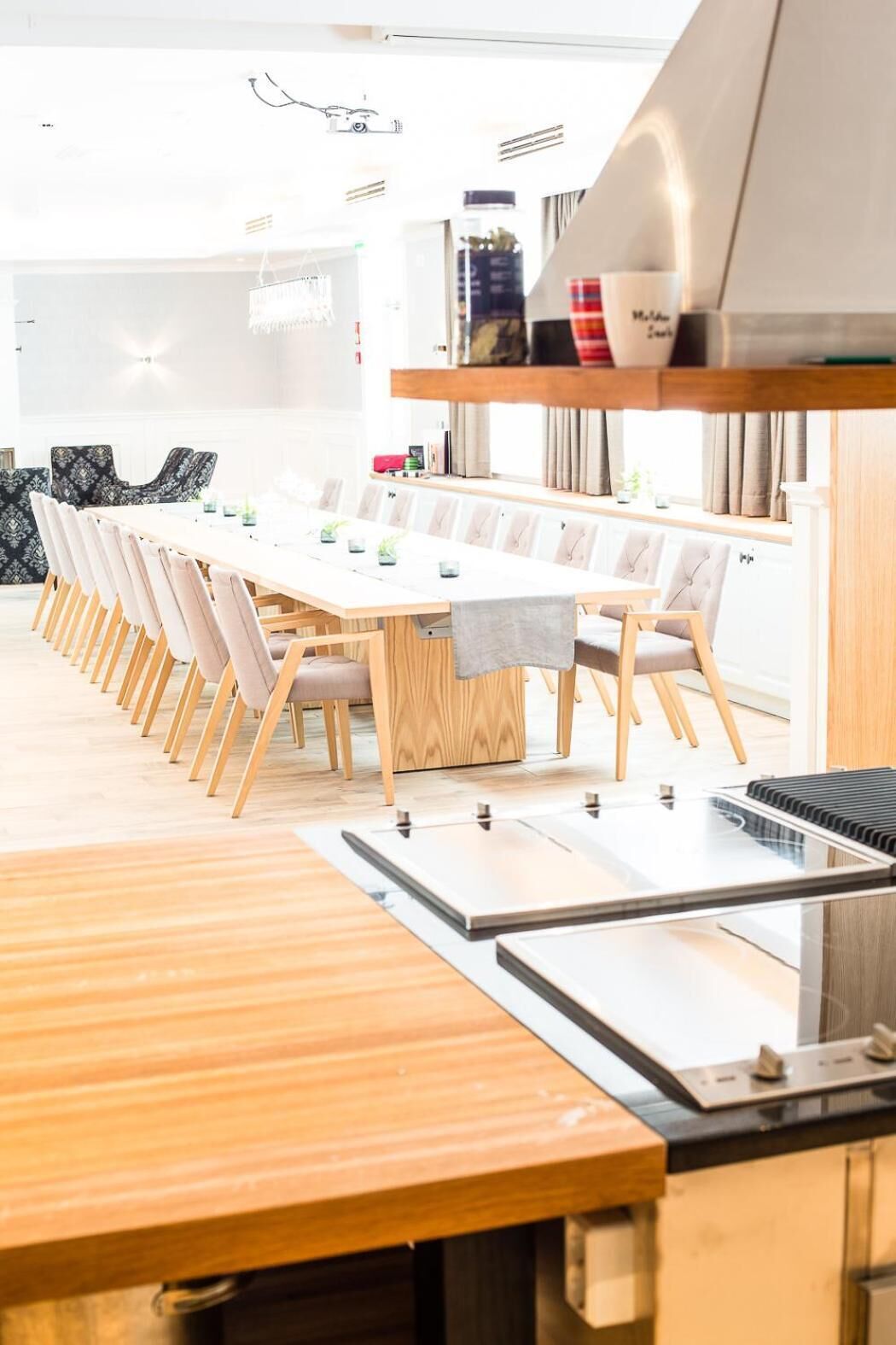 A modern kitchen with a long dining table, wooden chairs, and a built-in stove.