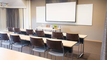 Un salón de conferencias con una pizarra grande, varias mesas y sillas dispuestas para reuniones.