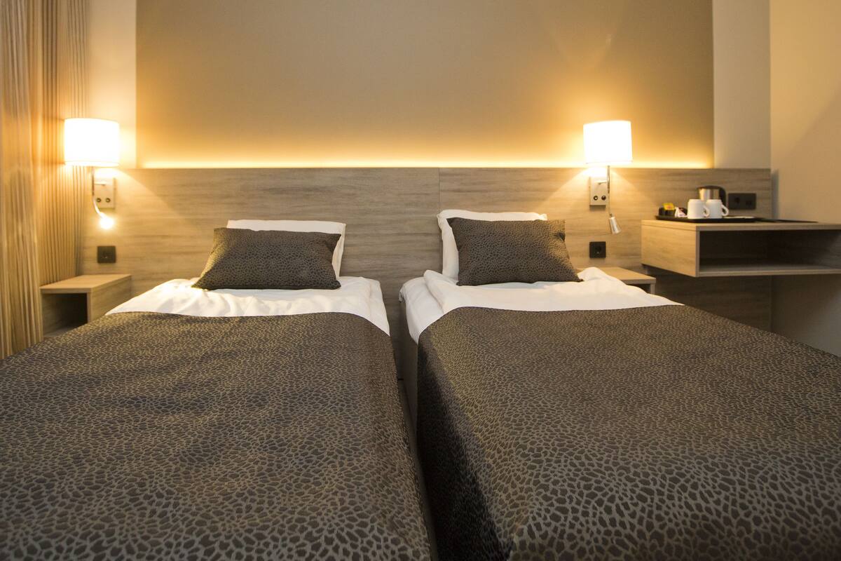Une chambre d’hôtel avec deux lits, chacun recouvert d’une couvre-lit à motifs léopard et agrémenté d’oreillers assortis. On y trouve des lampes de chevet, une table de chevet et une petite table avec une tasse et un livre.