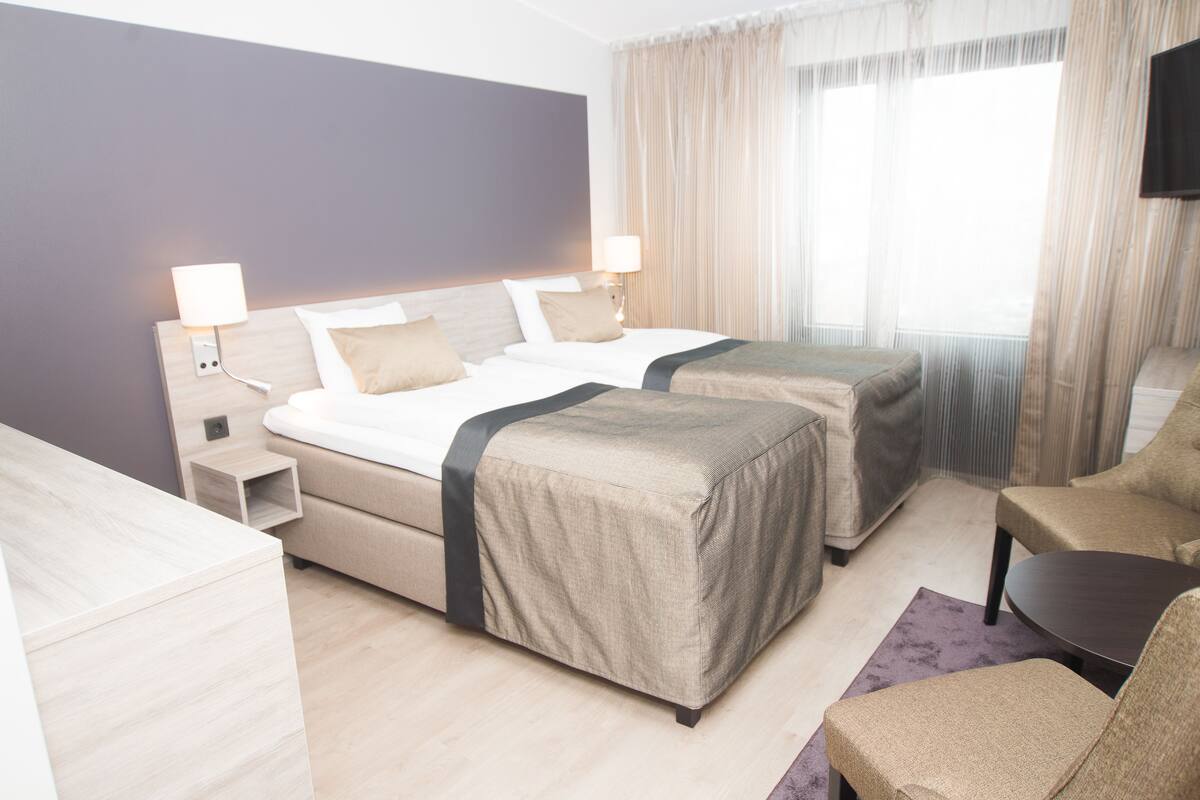 Une chambre d’hôtel avec deux lits, un bureau, une chaise et une télévision.