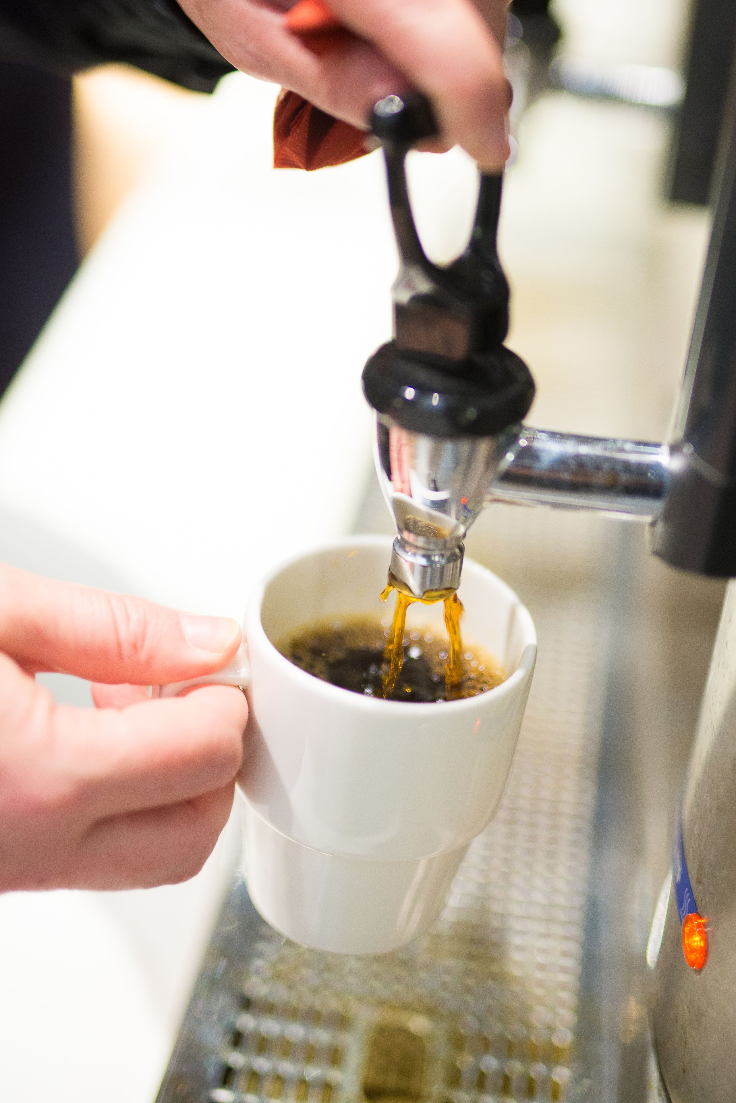 Una mano sostiene una taza blanca bajo una máquina de café que vierte café en la taza.