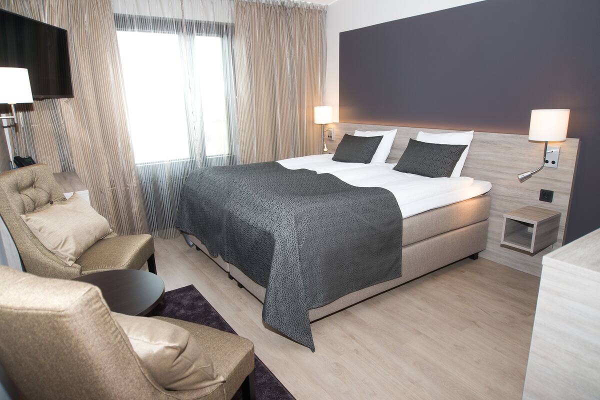 Une chambre d’hôtel moderne avec un grand lit, deux lampes de chevet, un téléviseur à écran plat, un canapé et une petite table d’appoint.