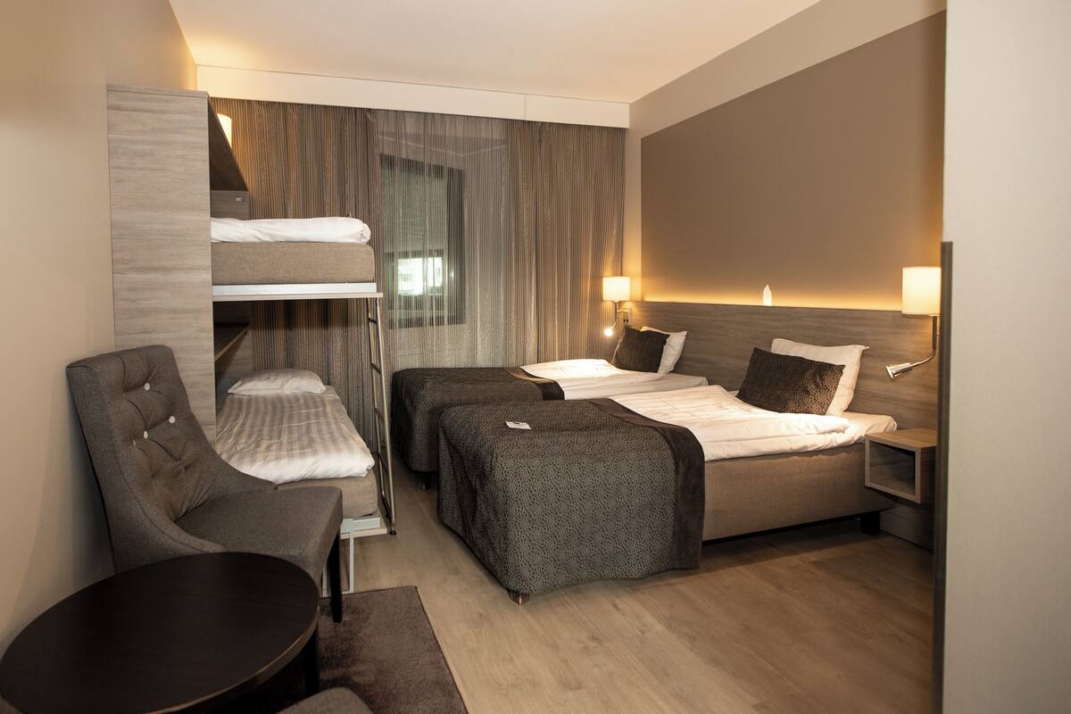 Une chambre d’hôtel équipée d’un lit superposé, d’un lit simple, d’une chaise, d’une table et d’une lampe de chevet.