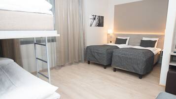 Habitación de hotel con literas, dos camas individuales, una mesita de noche con lámpara y un ventanal con cortinas.