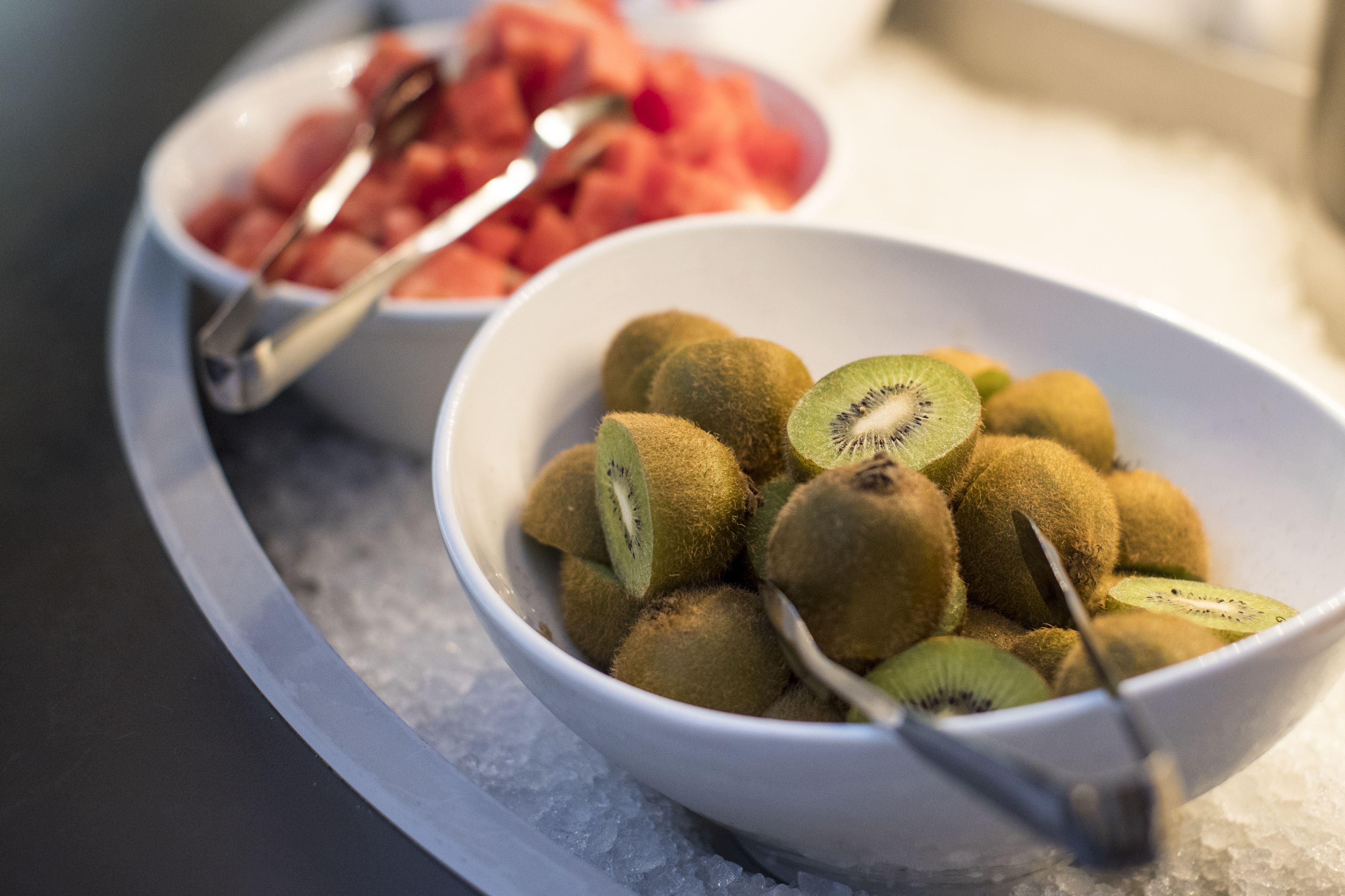 Two bowls of fruit on a tray with ice.