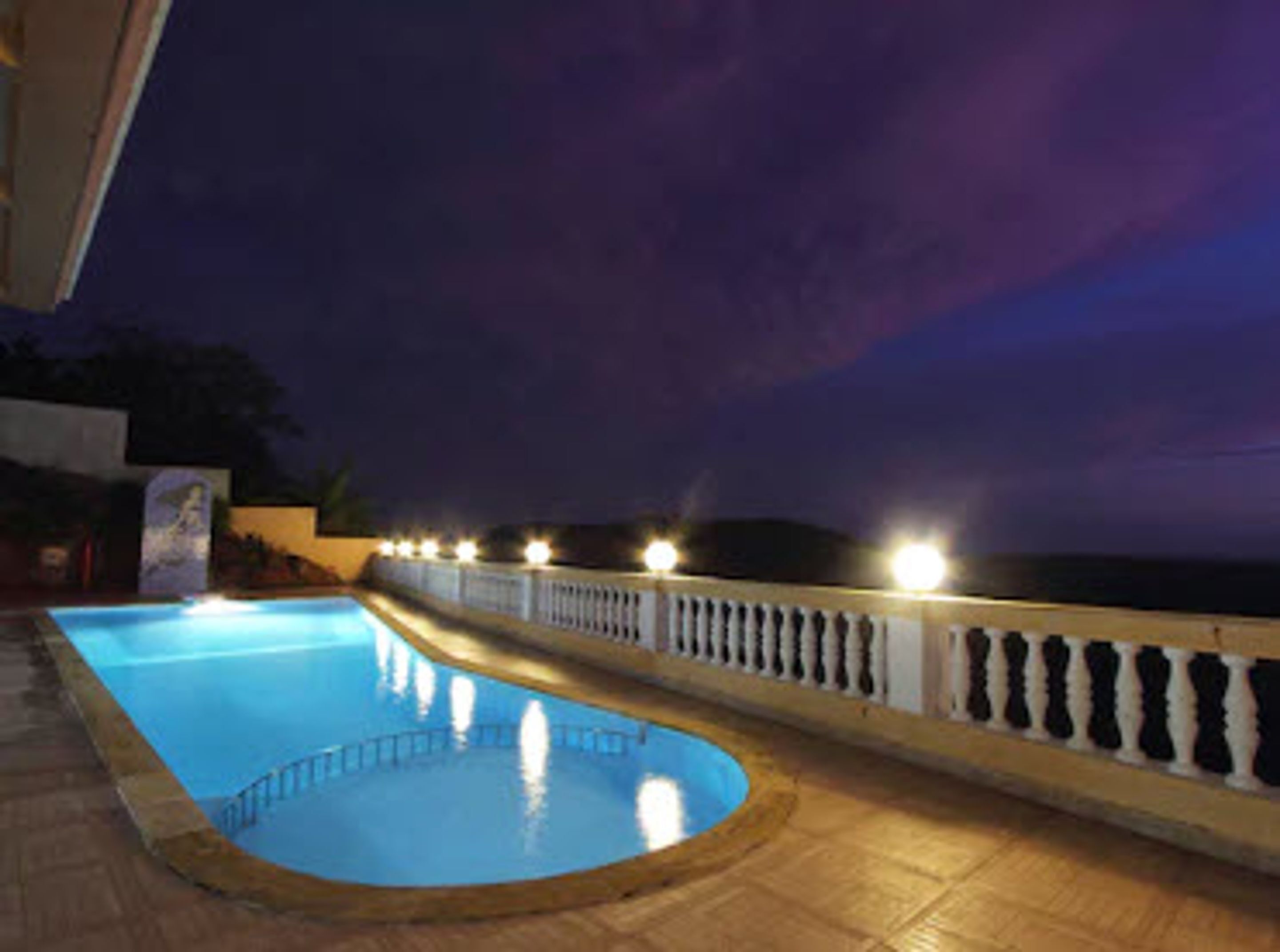 Une piscine dotée d’une balustrade blanche et d’éclairages le long du bord, entourée d’une terrasse dallée.