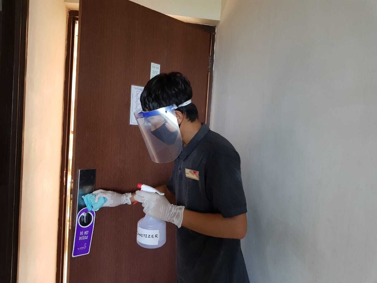 Iemand maakt een deurklink schoon met een sprayfles en een doek.