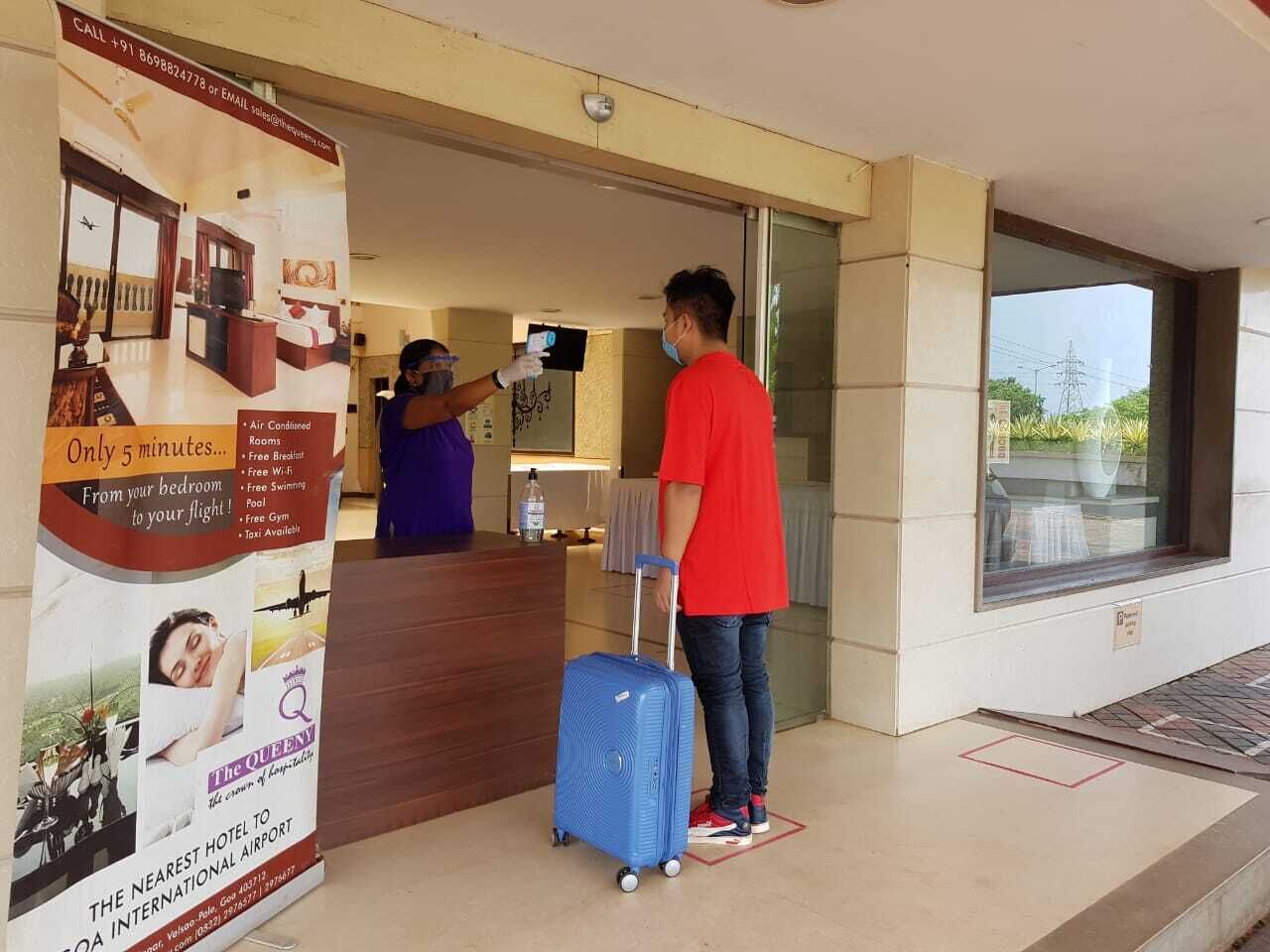Zona de recepción de hotel con un mostrador de madera, un cartel que anuncia servicios como habitaciones con aire acondicionado y Wi-Fi gratuito, y una persona con una maleta azul.