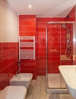 Un baño moderno con baldosas rojas, mampara de vidrio, bañera blanca y un bidé.