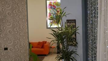 Una sala con papel tapiz estampado, un sofá naranja, una planta en maceta y una pared con una cita motivacional.