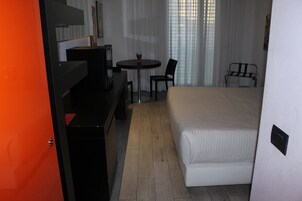 Una habitación de hotel con una cama, un escritorio con silla, una mesita con silla y una ventana con cortinas.