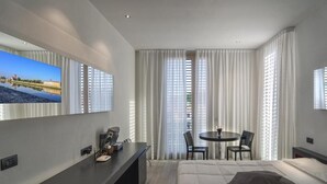 A modern hotel room with a large bed, a desk with a chair, a small table with chairs, and a TV mounted on the wall. - Blue Shades Aparthotel (Pisa)