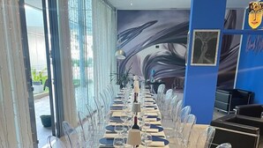 A long dining table set with clear chairs, a bottle of wine, and a mural on the wall. - Blue Shades Aparthotel (Pisa)