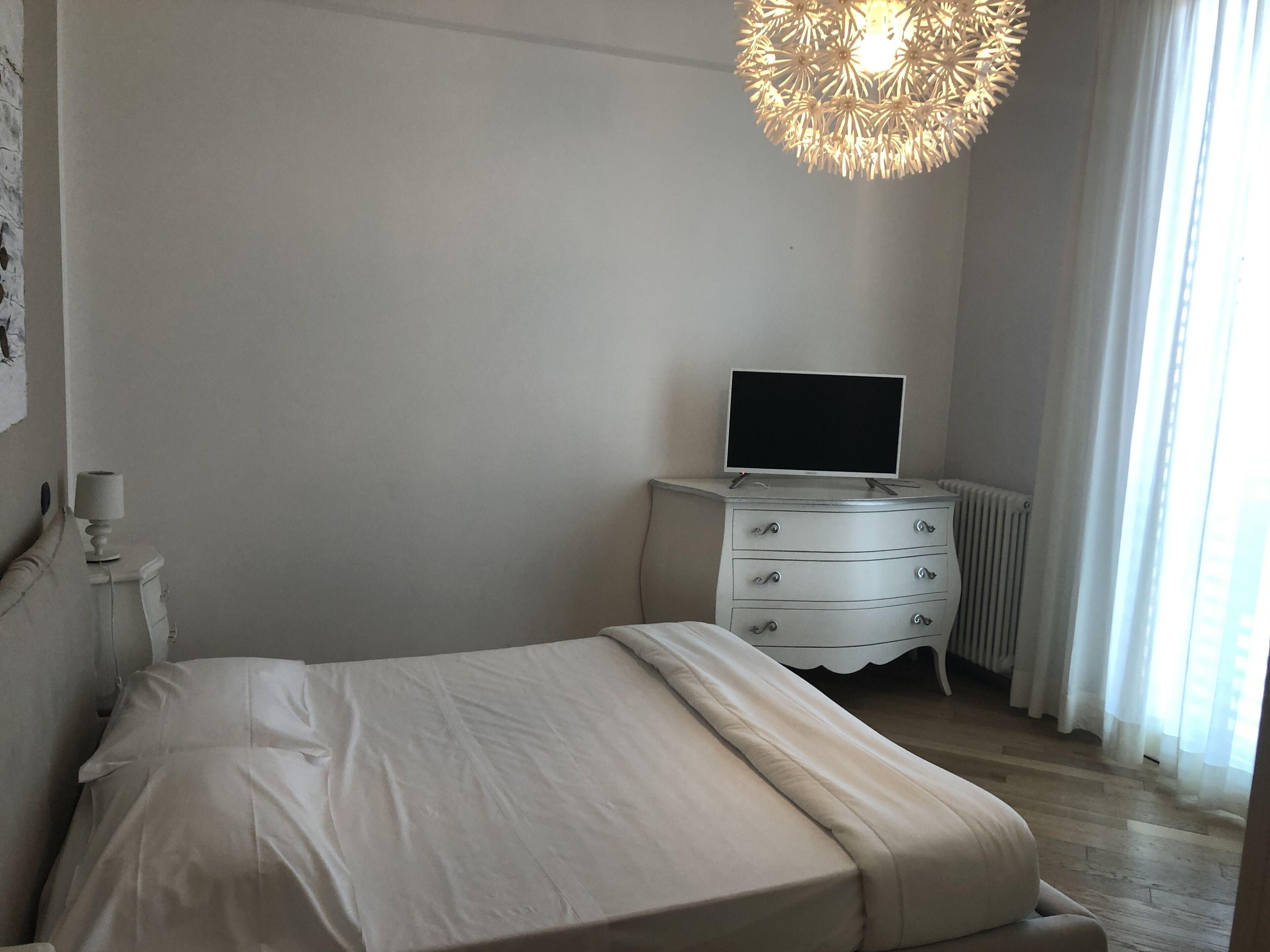 A minimalist bedroom with a bed, a dresser, a TV, and a radiator.