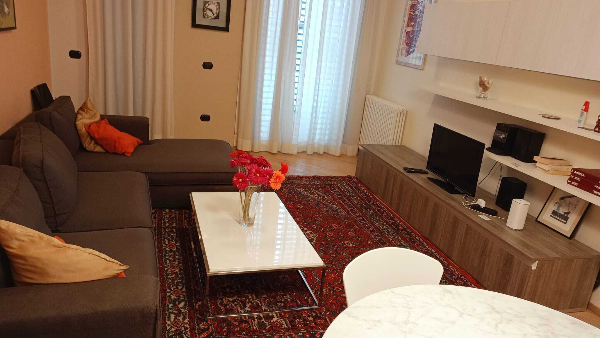 A living room with a sofa, a coffee table with flowers, a TV, and a bookshelf.
