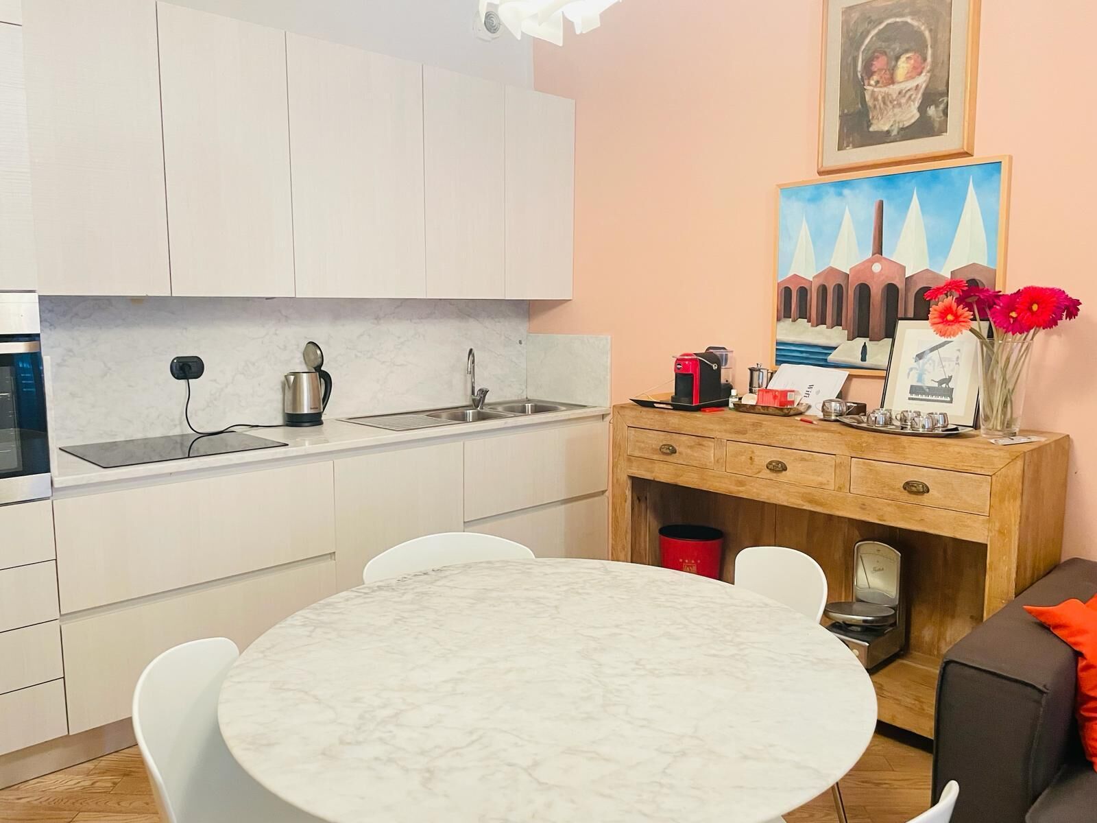 Eine kleine Küche mit weißen Schränken, einer Marmorarbeitsplatte und einem Holzsideboard mit einer Kaffeemaschine.