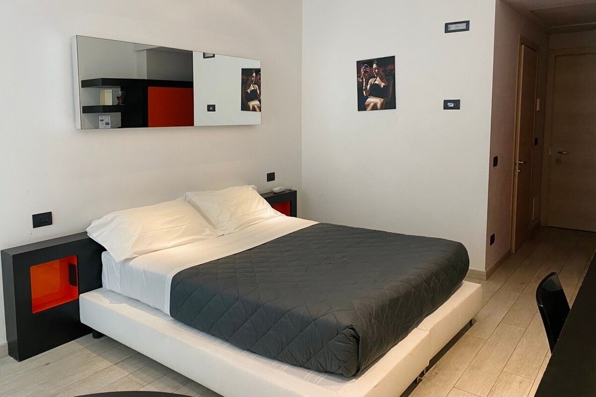 Un dormitorio moderno con cama, mesitas de noche, un espejo y una puerta.