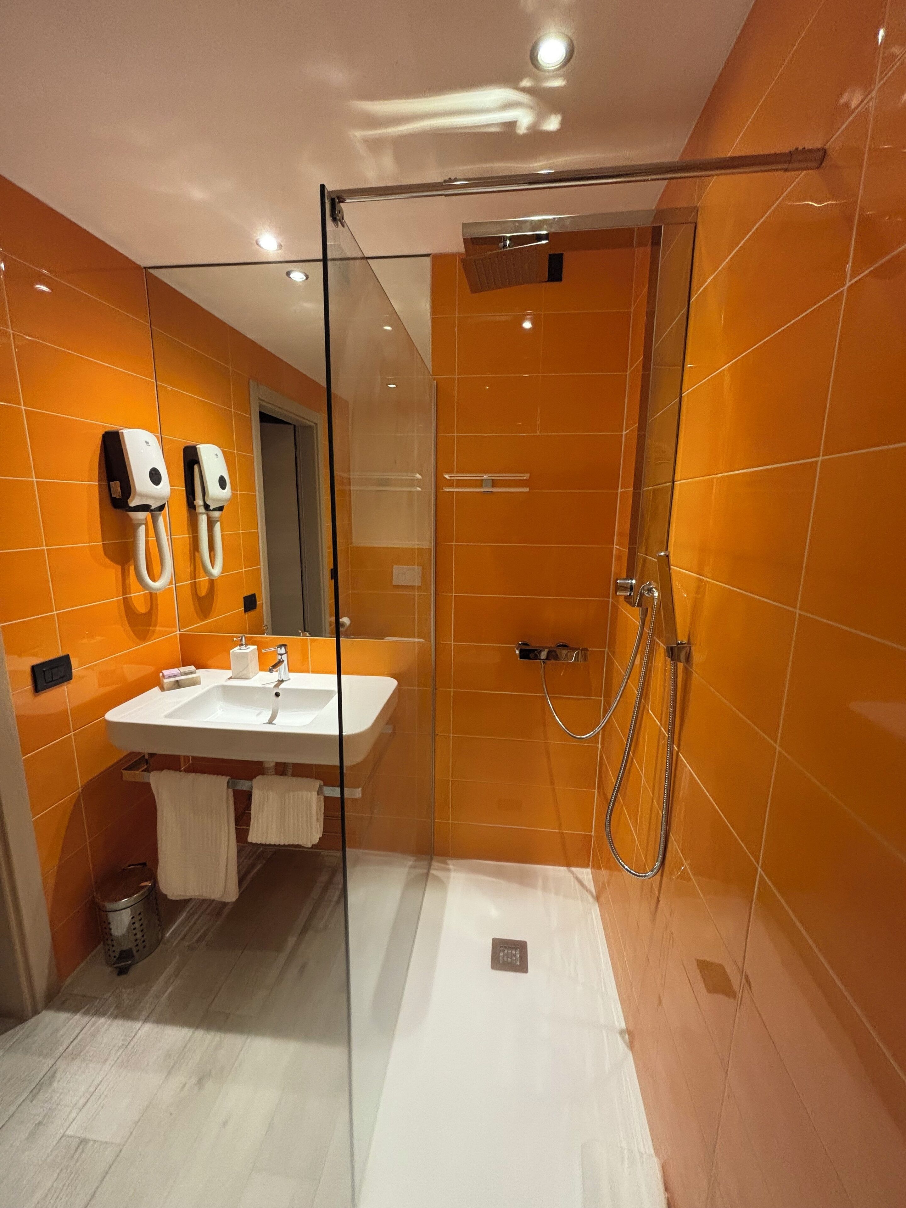A modern bathroom with a glass-enclosed shower, a white sink, and two hand dryers mounted on the wall.