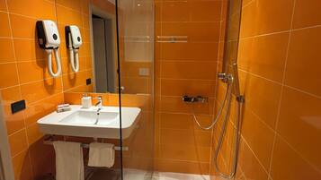 A modern bathroom with a glass-enclosed shower, a white sink, and two hand dryers mounted on the wall.