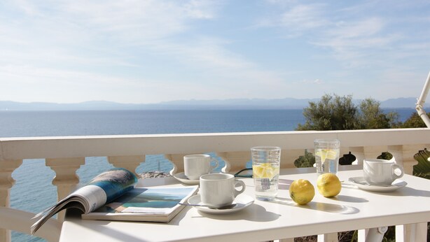A table with a book, two cups, a glass of water, and lemons on a balcony overlooking the sea. - Apollon Apartments (West Mani)