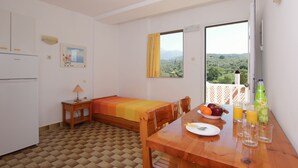 A small room with a bed, a table with breakfast, a window with a view, and a refrigerator. - Apollon Apartments (West Mani)