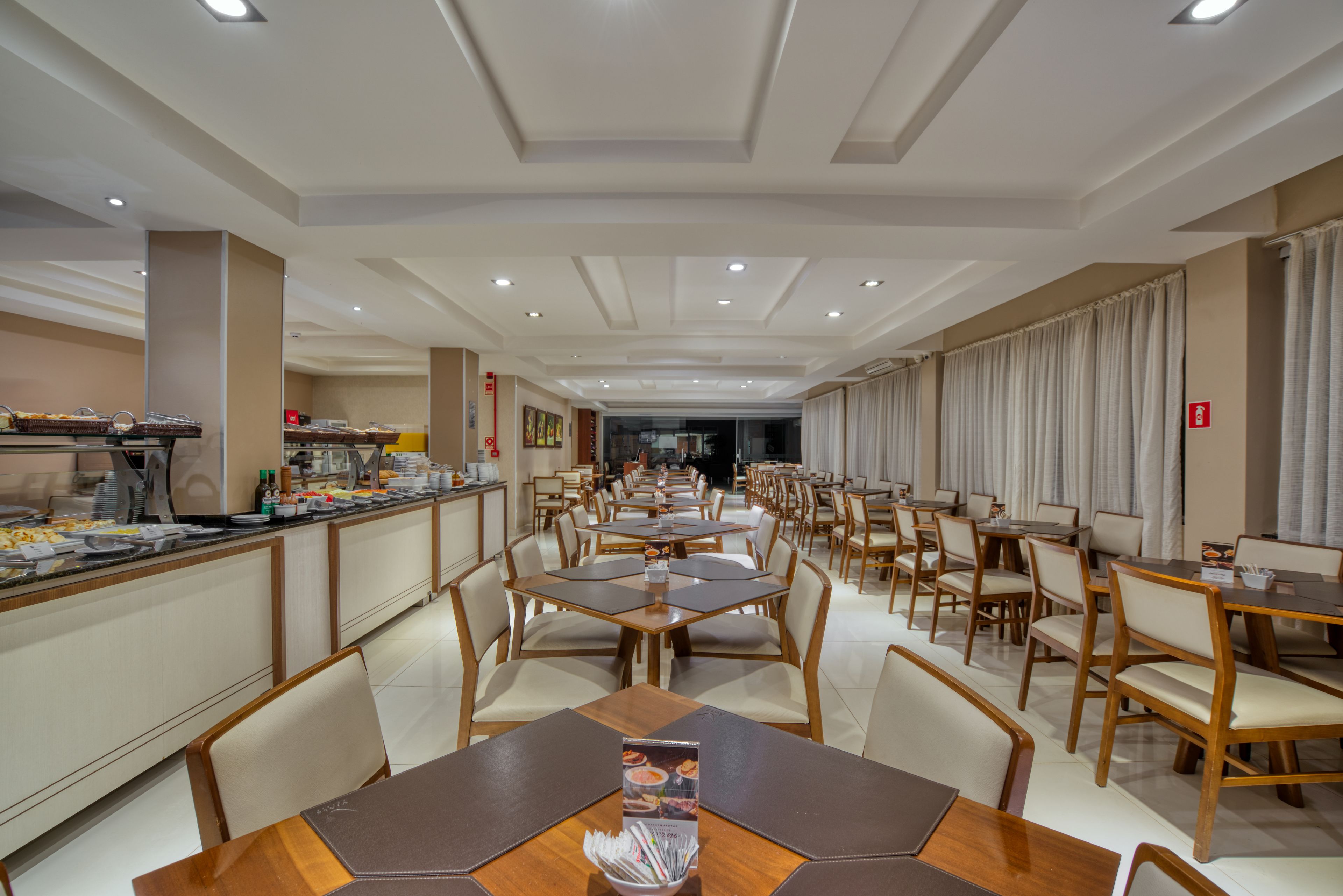 Een ruime eetruimte met meerdere tafels en stoelen, een buffet en een modern plafondontwerp.