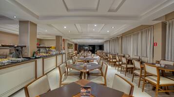 Een ruime eetruimte met meerdere tafels en stoelen, een buffet en een modern plafondontwerp.