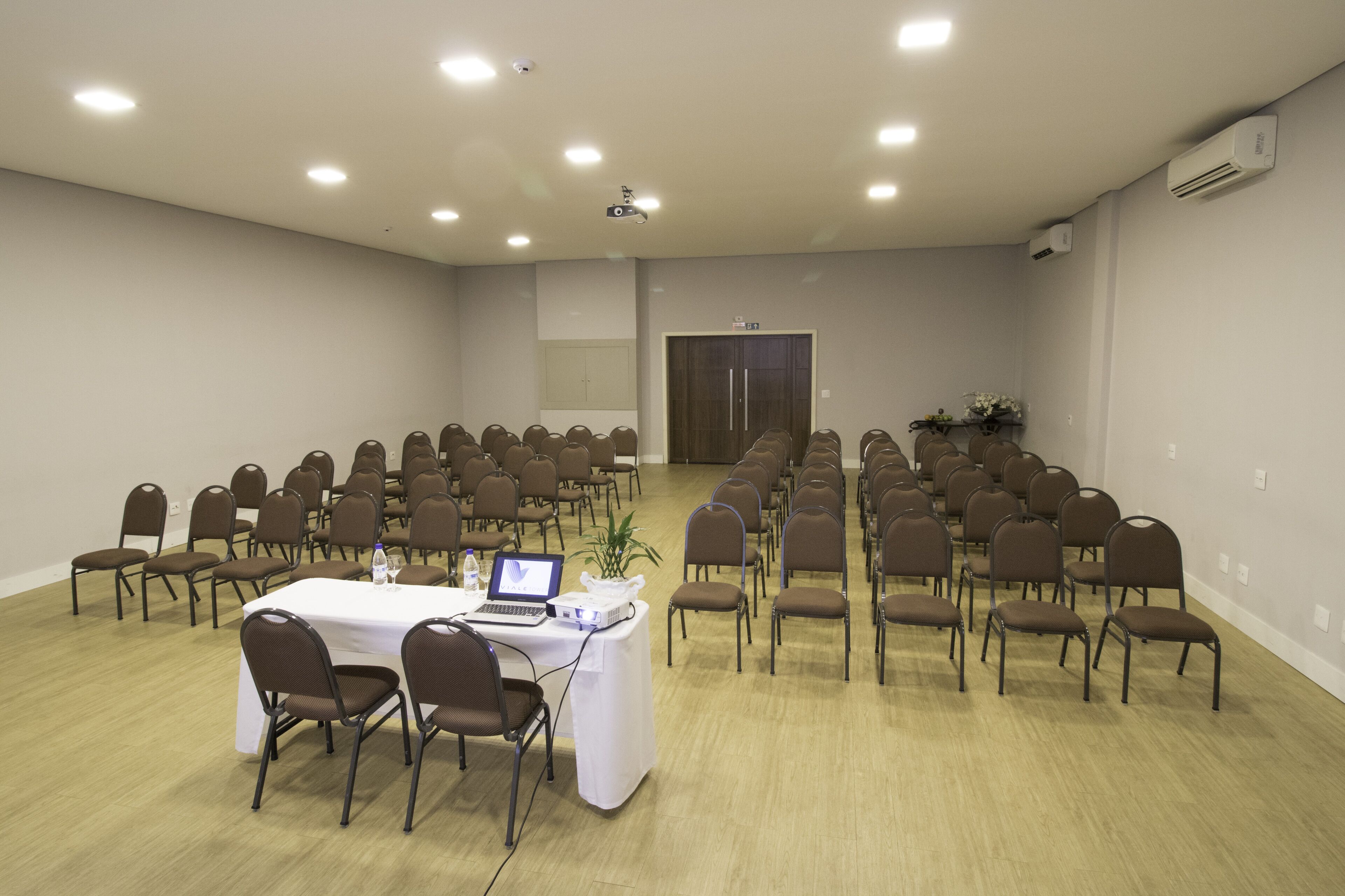 Une salle de conférence avec des rangées de chaises, une table avec un ordinateur portable et un projecteur.