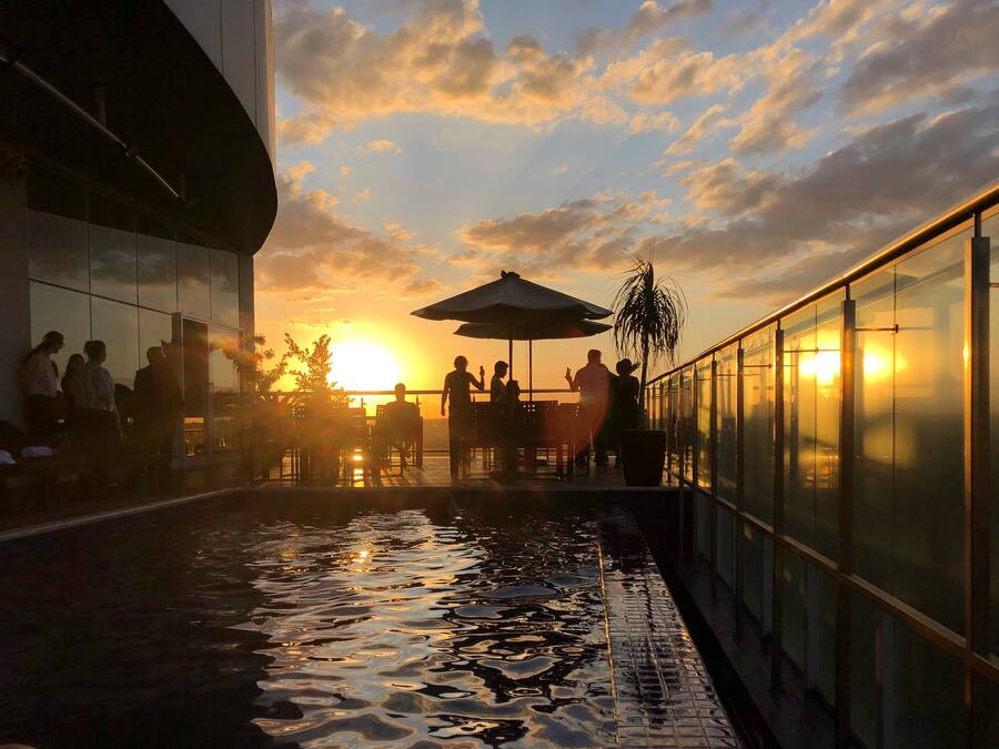 Ein Sonnenuntergangsblick von einer Dachterrasse mit Pool, Sitzgelegenheiten im Freien und einer Glasreling.