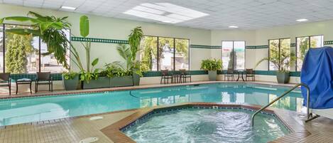 Una piscina interior con jacuzzi, rodeada de plantas en macetas y zonas de estar.