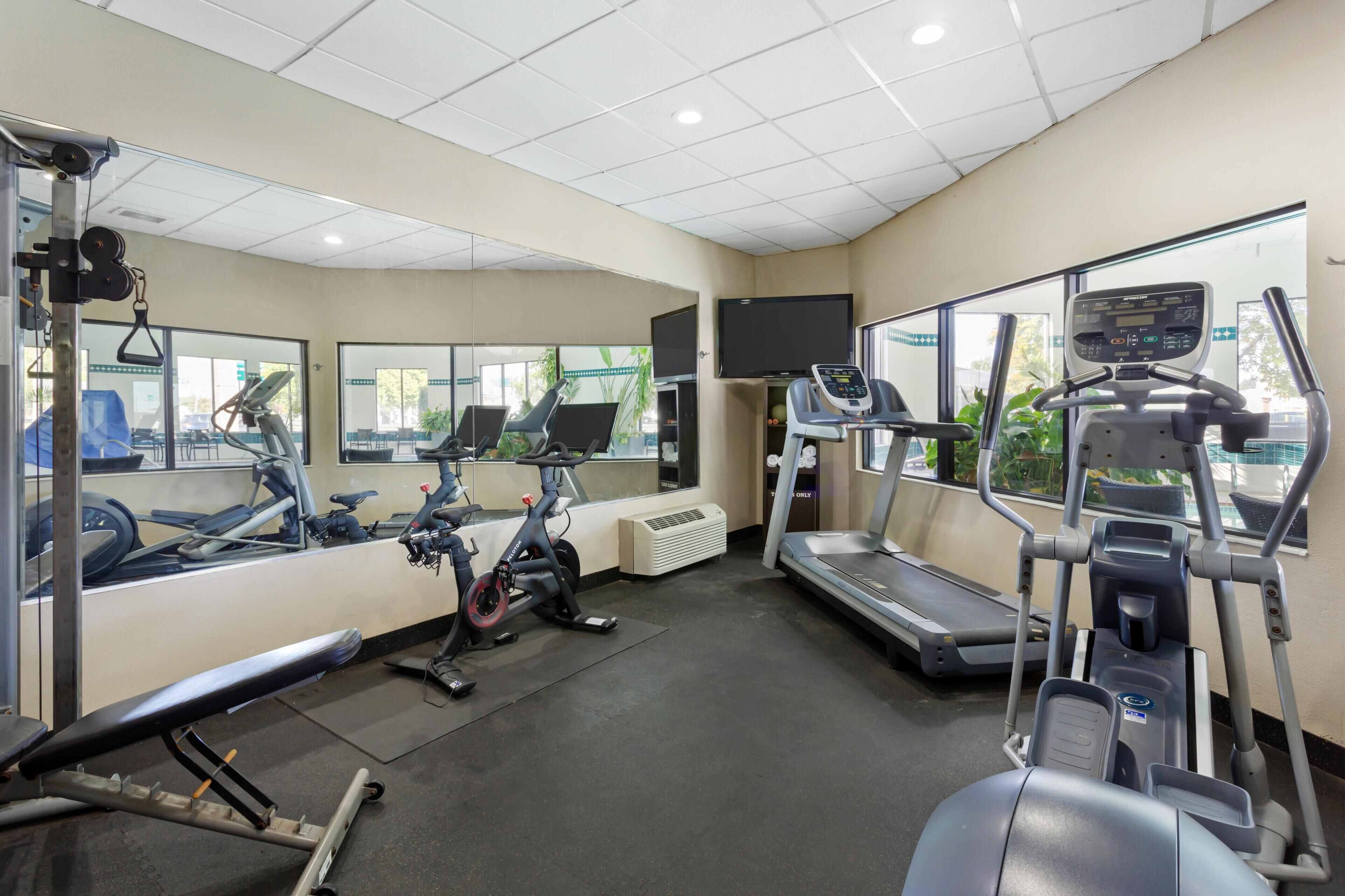 Une salle de sport équipée de matériel d’exercice, d’un téléviseur et de grandes fenêtres.