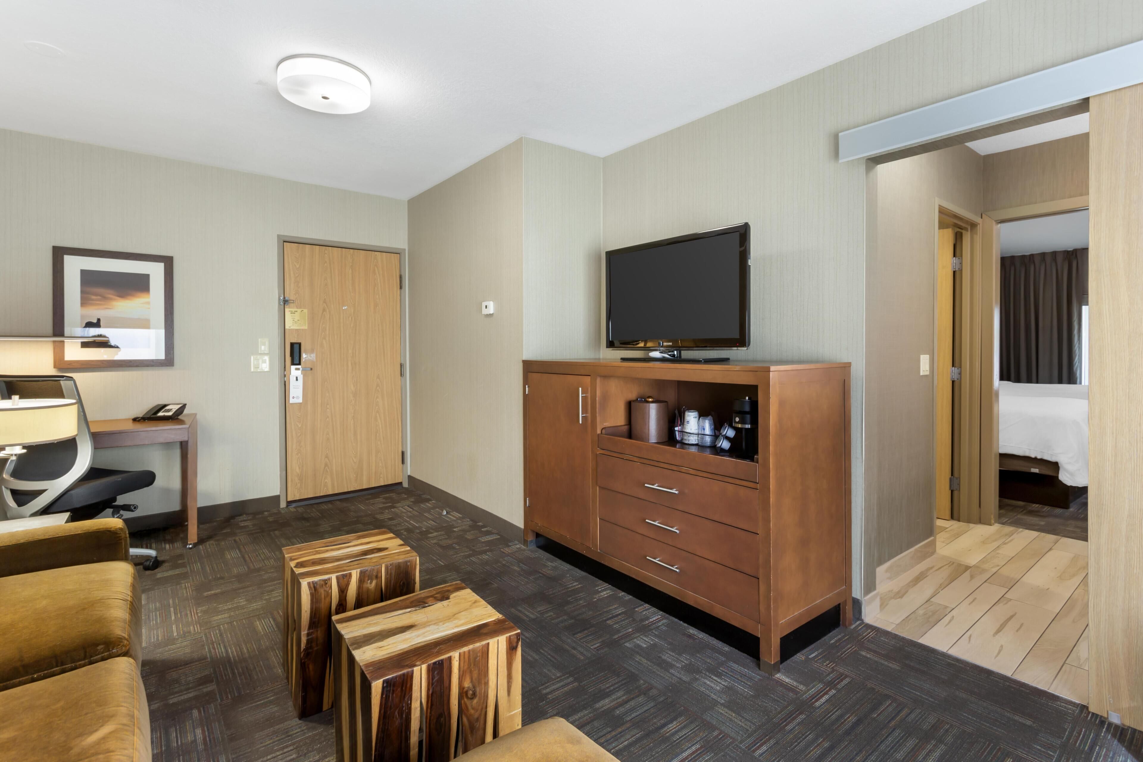 A hotel room with a wooden cabinet, a television, a desk with a chair, a bed, and a small wooden table.