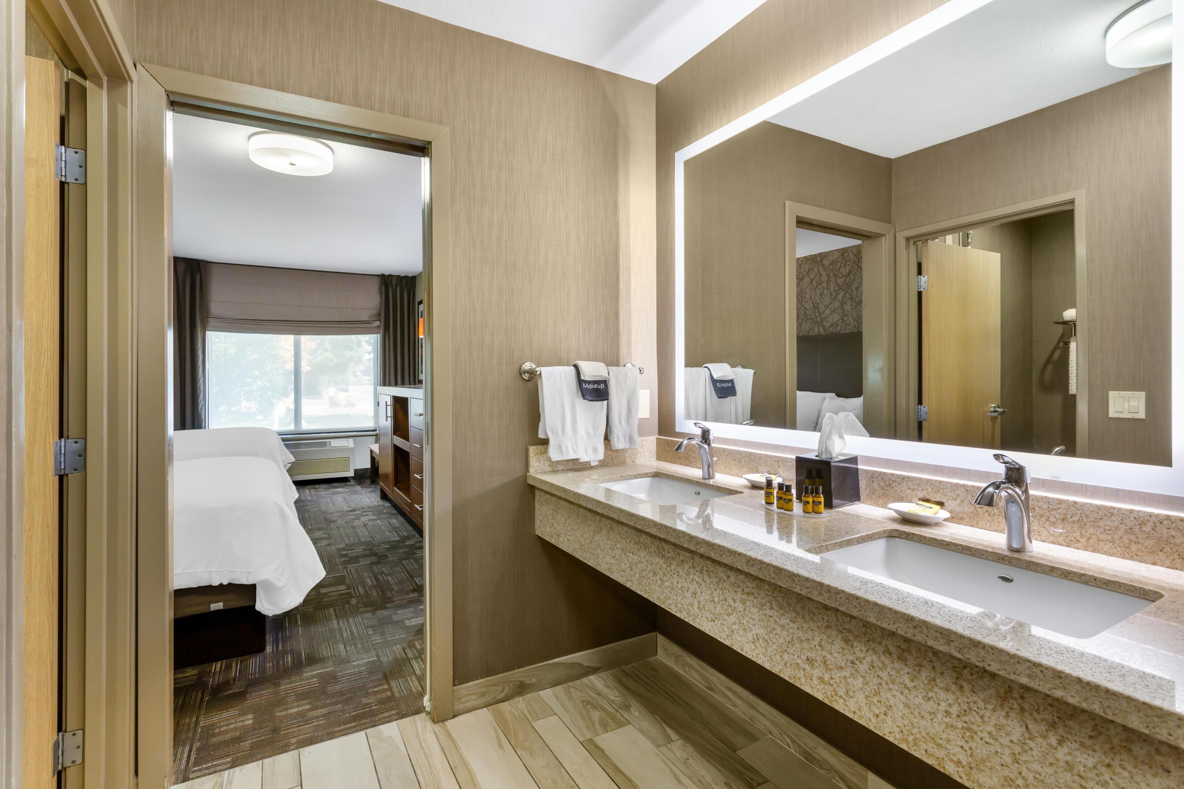 A hotel bathroom with a large mirror, two sinks, and a shower area.
