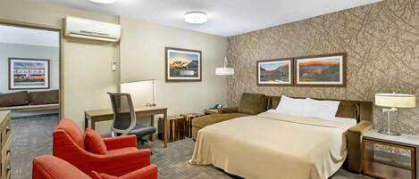 A hotel room with a bed, two bedside tables, a desk with a chair, a sofa, and two red armchairs.