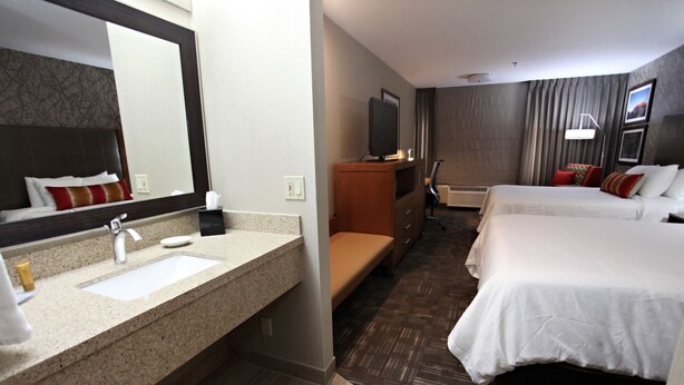 A hotel room with a large mirror, a sink, a television, two beds, and a bench. - Best Western Plus Cottontree Inn (Idaho Falls)