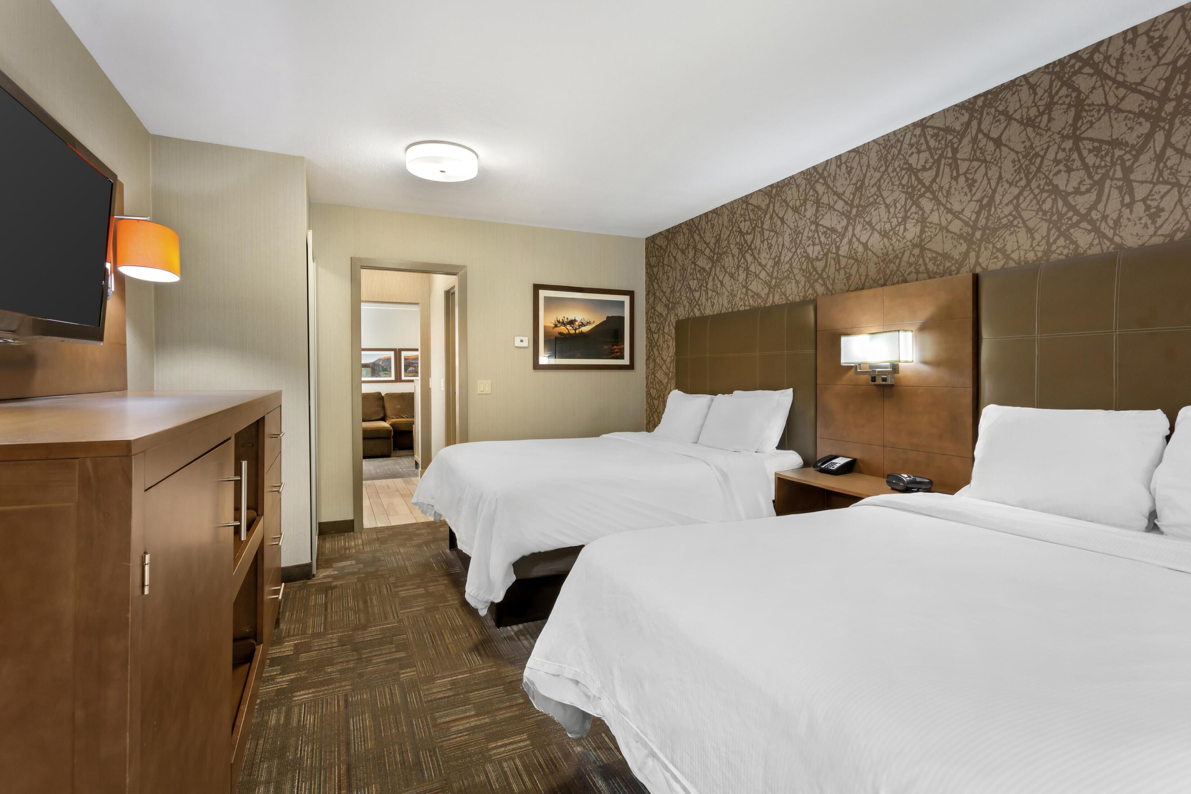A hotel room with two beds, a desk, a TV, and a bathroom visible through an open door.