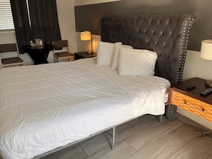 Une chambre d’hôtel avec un grand lit, une table de chevet avec une lampe, une chaise et une petite table avec une télécommande.