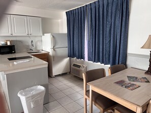 A compact kitchen with a refrigerator, microwave, and sink. There is a dining table with chairs and a lamp. - Sand Castle Motel (Daytona Beach Shores)