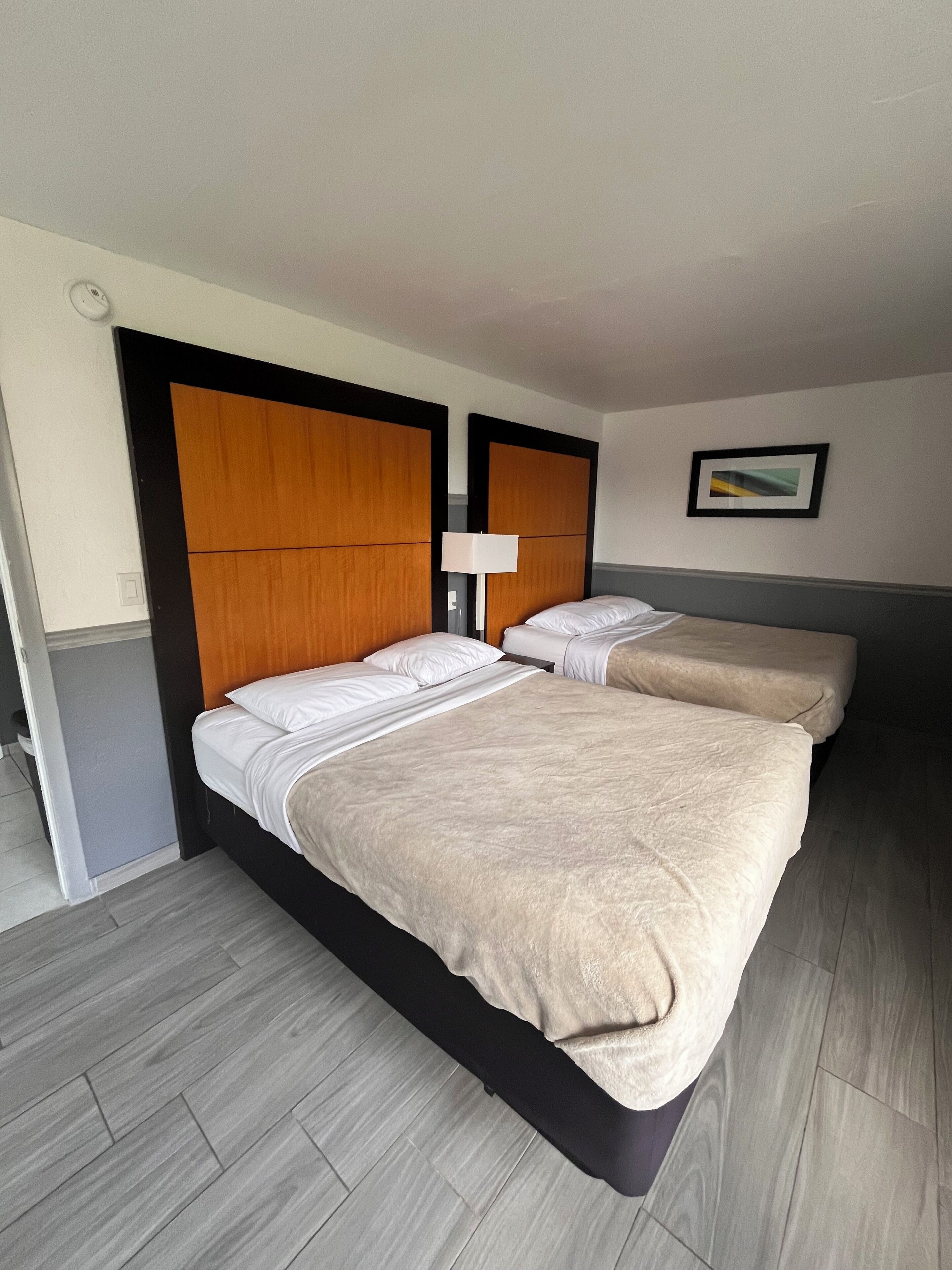 Une chambre d’hôtel avec deux lits, une table de chevet avec une lampe et un tableau encadré au mur.