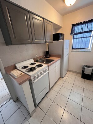 A compact kitchen with a stove, sink, and refrigerator. - Sand Castle Motel (Daytona Beach Shores)