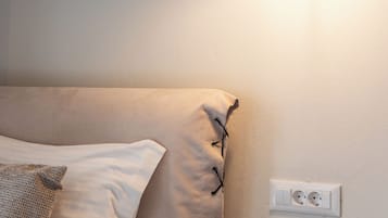 A neatly made bed with a pillow, a bedside table, and a wall socket.